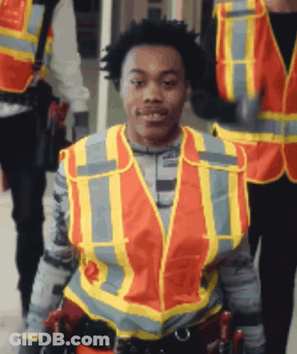 A Man Wearing An Orange And Yellow Safety Vest With The Letter T On It GIF
