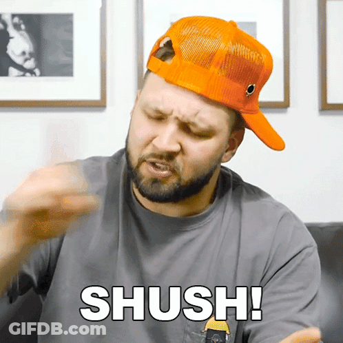 A Man Wearing An Orange Hat And A Grey Shirt Says " Shush " GIF