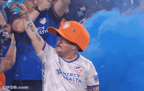 A Man Wearing An Orange Hat And A Mercy Health Shirt GIF