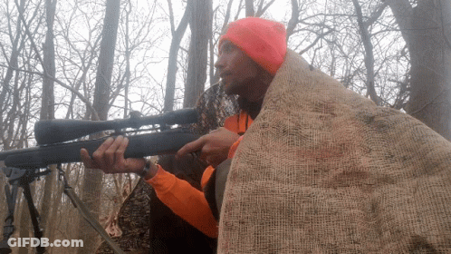 A Man Wearing An Orange Hat Is Holding A Rifle GIF