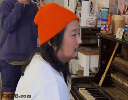 A Man Wearing An Orange Hat Is Playing The Piano GIF