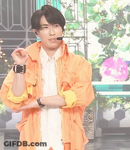 A Man Wearing An Orange Jacket And A White Shirt Is Standing With His Arms Crossed GIF