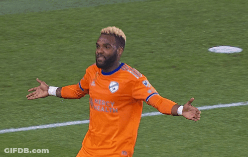 A Man Wearing An Orange Mercy Wealth Jersey Stands On A Soccer Field GIF