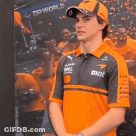A Man Wearing An Orange Shirt And A Hat Is Standing In Front Of A Picture Of A Crowd . GIF