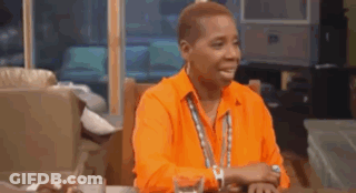 A Man Wearing An Orange Shirt Is Sitting At A Table With A Glass Of Water . GIF