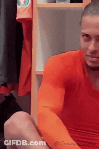 A Man Wearing An Orange Shirt Is Sitting In A Locker Room GIF