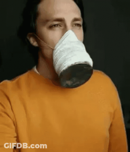 A Man Wearing An Orange Sweater Is Wearing A Mask On His Face . GIF