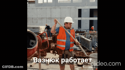 A Man Wearing An Orange Vest And A White Hard Hat Is Standing In Front Of A Concrete Mixer On A Construction Site GIF