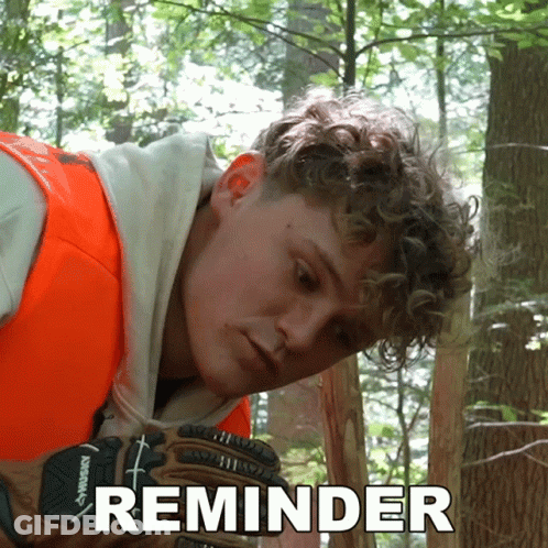A Man Wearing An Orange Vest And Husky Gloves Is Looking At Something In The Woods GIF