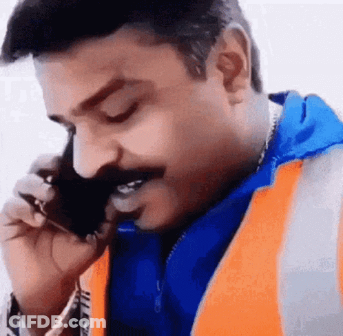 A Man Wearing An Orange Vest Is Talking On A Cell Phone . GIF
