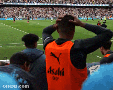 A Man Wearing An Orange Vest That Says Asahi On It Watches A Soccer Game GIF
