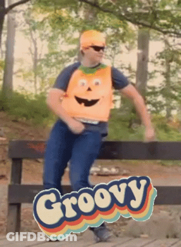 A Man Wearing An Orange Vest With A Face On It Is Dancing In Front Of A Groovy Sign GIF