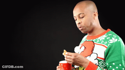 A Man Wearing An Ugly Christmas Sweater Is Holding A Cup And A Piece Of Food GIF