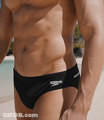A Man Wearing Black Speedo Swim Briefs Is Standing On A Beach GIF
