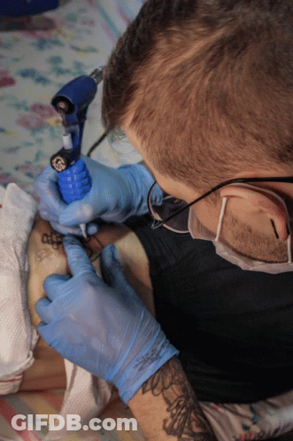 A Man Wearing Blue Gloves Is Getting A Tattoo On Someone 'S Leg GIF