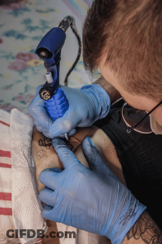 A Man Wearing Blue Gloves Is Getting A Tattoo On Someone 'S Leg GIF