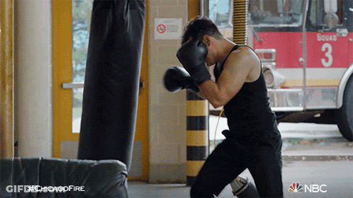 A Man Wearing Boxing Gloves Is Practicing In Front Of A Fire Truck With The Number 3 On It GIF