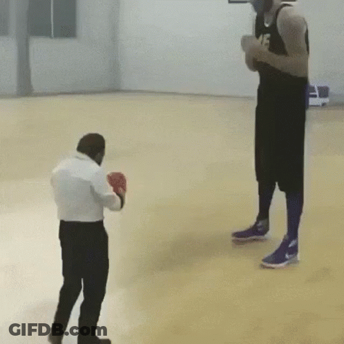 A Man Wearing Boxing Gloves Is Standing Next To A Man Wearing Basketball Shorts On A Basketball Court . GIF