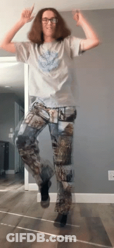 A Man Wearing Camo Pants Is Jumping In The Air With His Hands In The Air GIF