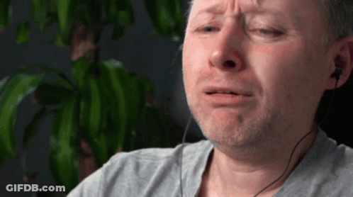 A Man Wearing Ear Buds And A Gray Shirt Is Crying GIF