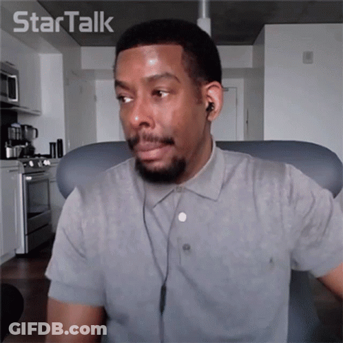 A Man Wearing Ear Buds And A Grey Shirt Is Sitting In Front Of A Star Talk Logo GIF