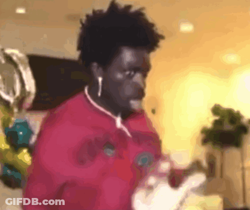 A Man Wearing Ear Buds And A Red Shirt Is Standing In A Room . GIF