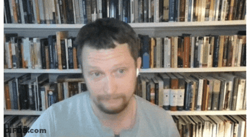 A Man Wearing Ear Buds Is Standing In Front Of A Bookshelf GIF