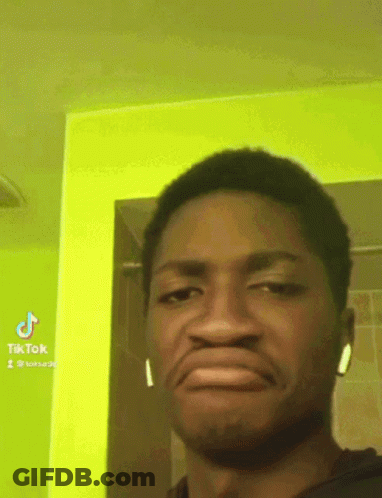A Man Wearing Ear Buds Making A Funny Face In Front Of A Green Wall GIF