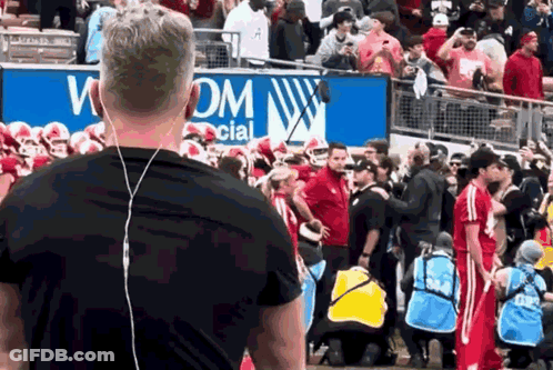 A Man Wearing Ear Buds Stands In Front Of A Sign That Says Wom Social GIF