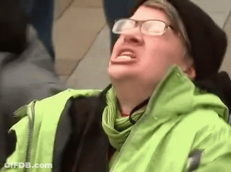 A Man Wearing Glasses , A Green Jacket And A Black Hat Is Making A Funny Face . GIF