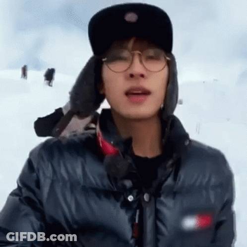 A Man Wearing Glasses , A Hat And A Jacket Is Standing In The Snow . GIF