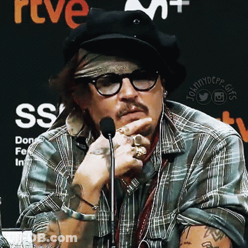 A Man Wearing Glasses And A Bandana Talks Into A Microphone In Front Of A Sign That Says Rtve Ss GIF