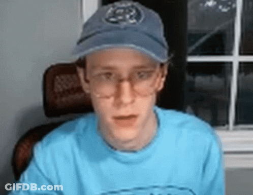 A Man Wearing Glasses And A Baseball Cap Is Sitting In Front Of A Window . GIF