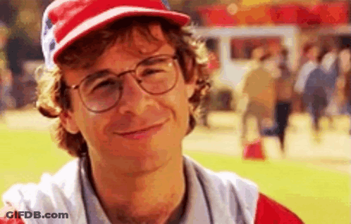A Man Wearing Glasses And A Baseball Cap Is Smiling At The Camera . GIF