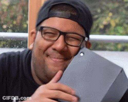A Man Wearing Glasses And A Baseball Cap Is Smiling While Holding A Tablet . GIF