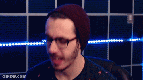 A Man Wearing Glasses And A Beanie Is Standing In Front Of Blue Lights GIF