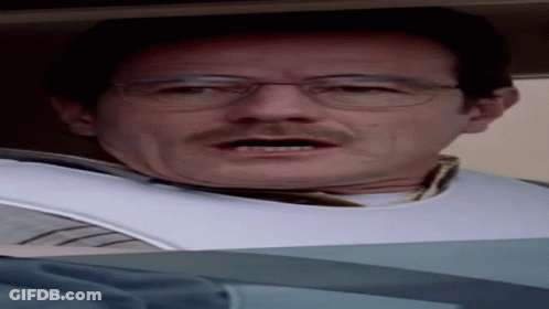 A Man Wearing Glasses And A Bib On His Neck Looks At The Camera GIF
