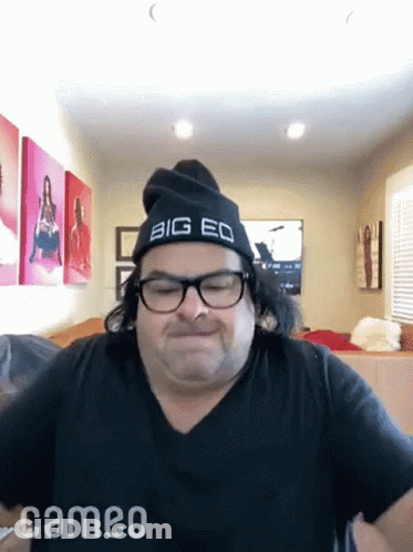 A Man Wearing Glasses And A Big Eq Hat Is Making A Funny Face . GIF