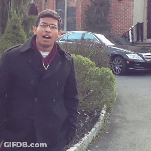 A Man Wearing Glasses And A Black Coat Stands In Front Of A Black Car GIF