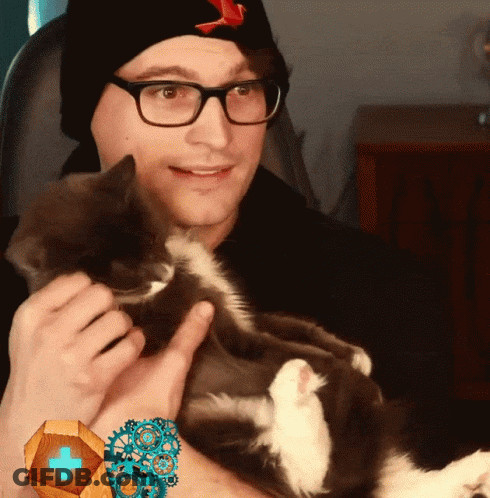 A Man Wearing Glasses And A Black Hat Holds A Cat In His Arms GIF