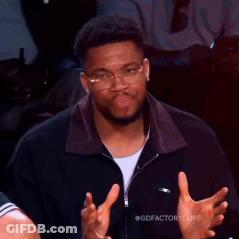 A Man Wearing Glasses And A Black Jacket Is Making A Funny Face While Giving A Thumbs Up . GIF