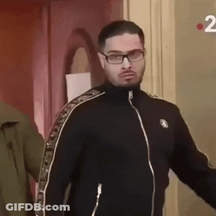 A Man Wearing Glasses And A Black Jacket Is Standing Next To A Door . GIF