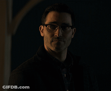 A Man Wearing Glasses And A Black Jacket Stands In The Dark GIF