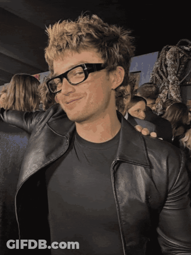 A Man Wearing Glasses And A Black Leather Jacket Smiles GIF