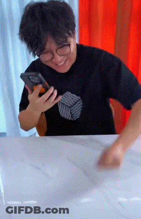 A Man Wearing Glasses And A Black Shirt Holds A Cell Phone In His Hand GIF