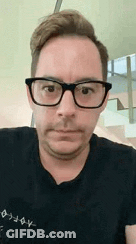 A Man Wearing Glasses And A Black Shirt Is Making A Face . GIF