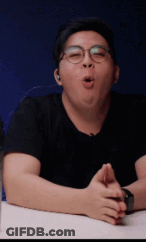 A Man Wearing Glasses And A Black Shirt Is Sitting At A Table With His Mouth Open GIF