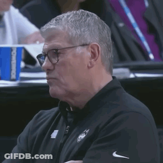 A Man Wearing Glasses And A Black Shirt Is Sitting In A Stadium Watching A Game GIF