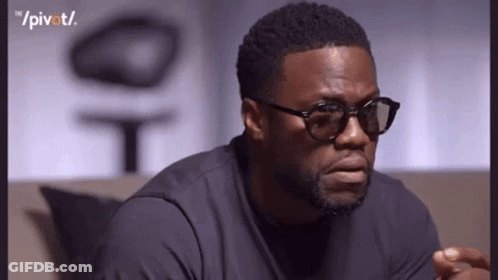 A Man Wearing Glasses And A Black Shirt Is Sitting On A Couch And Making A Funny Face . GIF