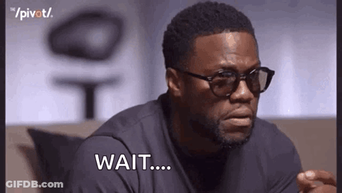 A Man Wearing Glasses And A Black Shirt Is Sitting On A Couch And Saying `` Wait ... '' . GIF